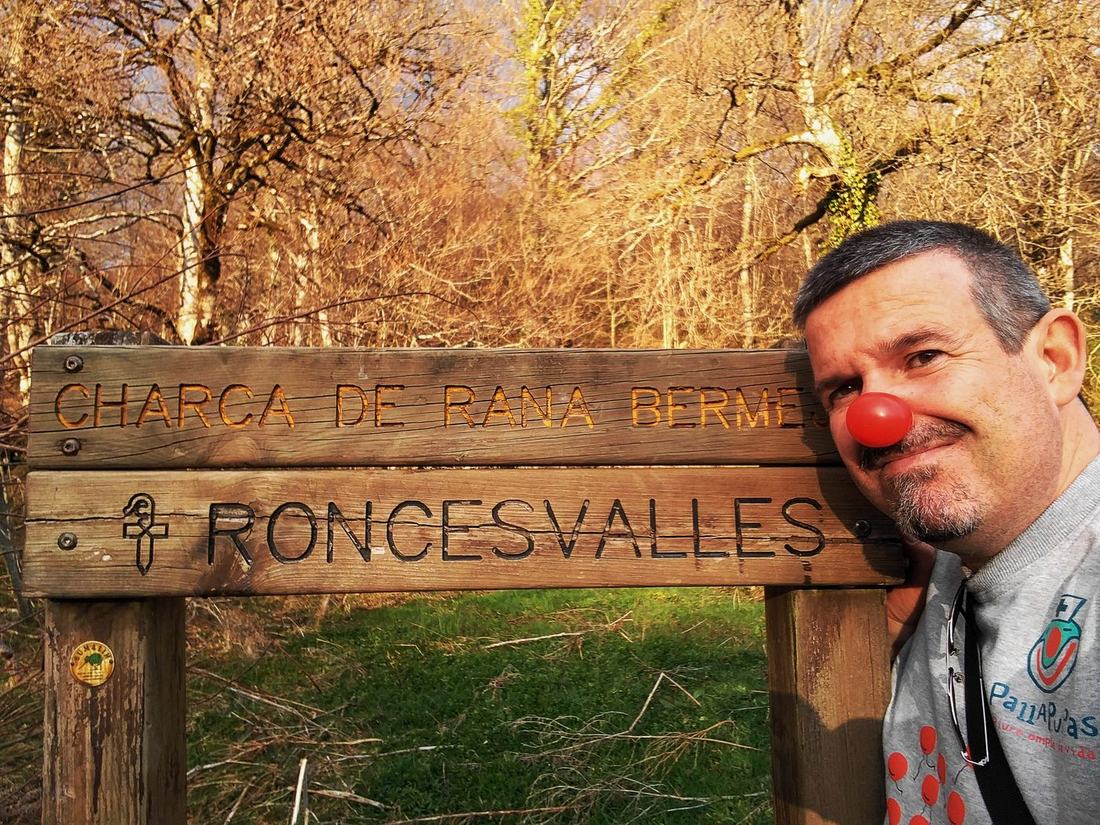 Francesc Esteve amb nas de pallasso i samarreta de Pallapupas al costat del cartell de Roncesvalles, inici del Camí de Santiago francès